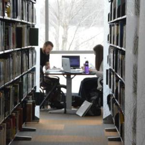 Two students sitting at a desk in front of a window at the library